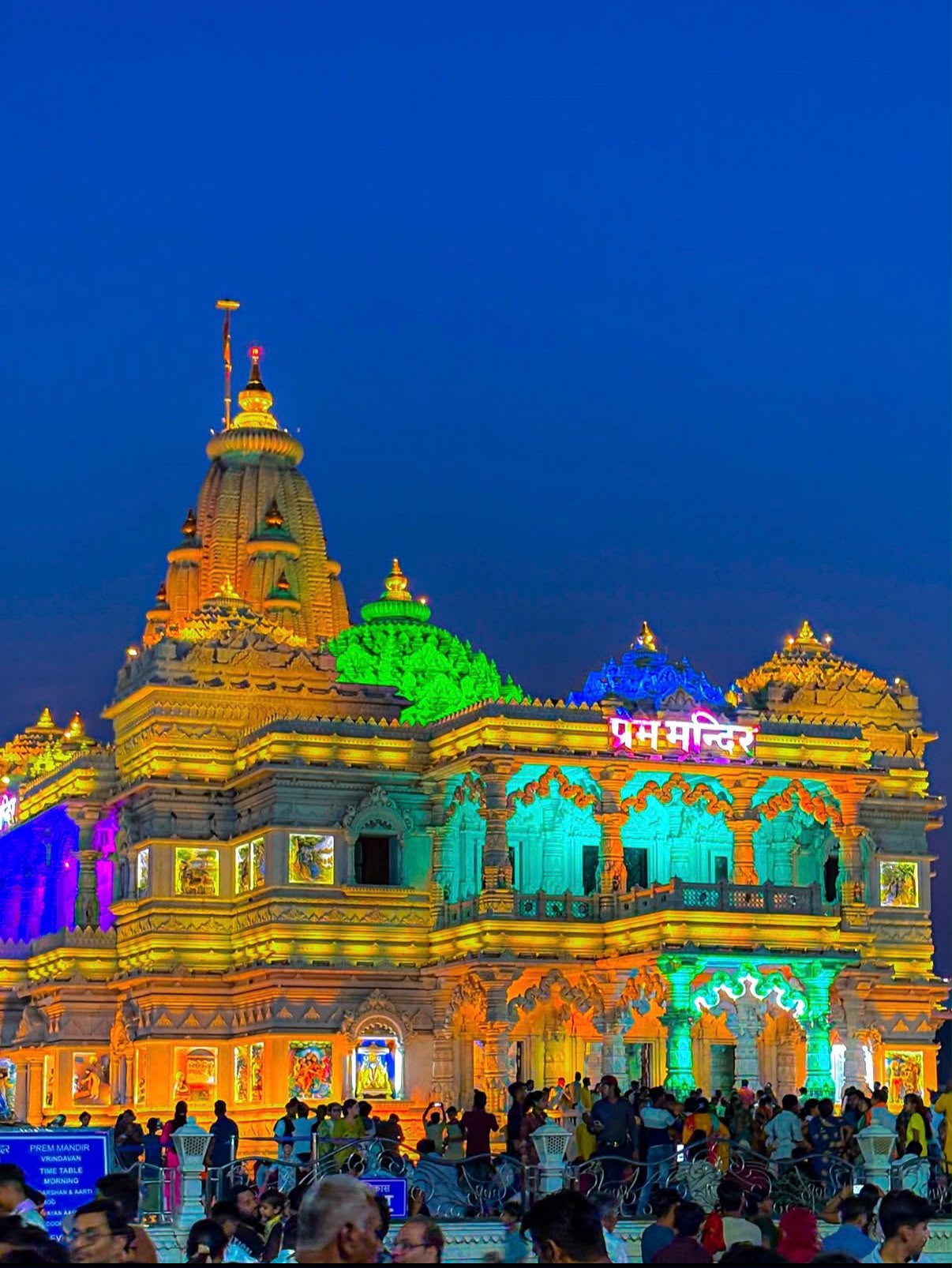 Prem Mandir in Vrindavan illuminated in gold, green, turquoise and blue at dusk