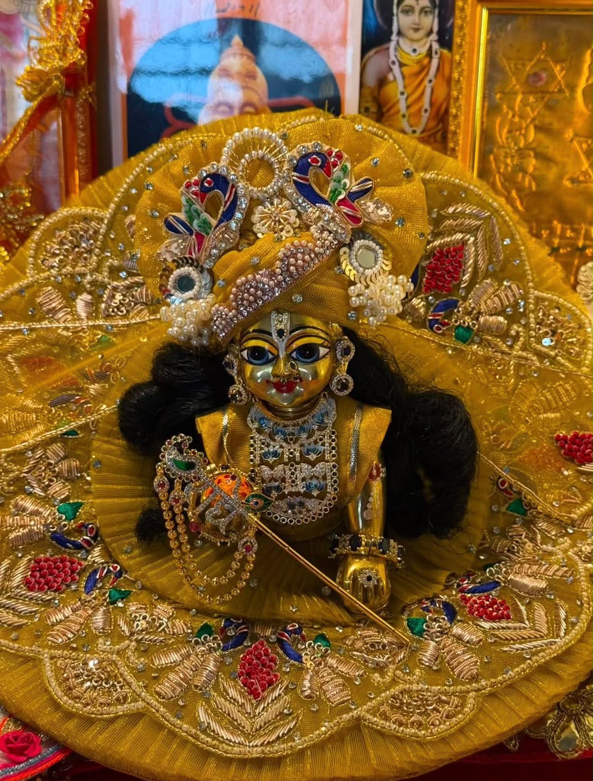 Laddu Gopal adorned in a golden yellow dress with pearl and peacock details